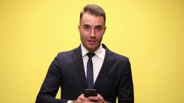 Genç yakışıklı iş adamı telefonuyla mesaj atıyor, başarıları tek yumruğuyla kutluyor sarı arka planda.