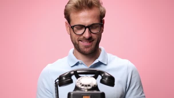 青いポロシャツのカジュアルな笑顔の男は古いロータリー電話を拾う 笑ってピンクの背景に親指をジェスチャーアップ — ストック動画