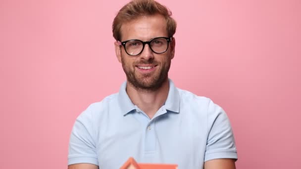 Sonriente Joven Casual Polo Azul Sosteniendo Casa Modelo Delante Cara — Vídeo de stock