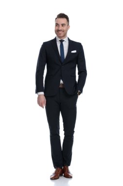 Çekici iş adamı gülümsüyor ve beyaz stüdyo arka planında dururken elini cebine atıyor.