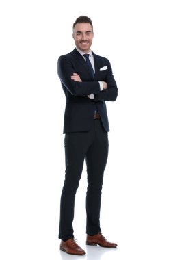 Beyaz stüdyo arka planında dururken elleri göğsünde katlanmış gülümseyen kendinden emin bir işadamı.