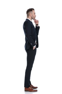 Beyaz stüdyo arka planında dururken çene ve cebinde el ele tutuşan iş adamının yan görünüşü