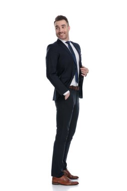 Beyaz stüdyo arka planında dikilirken gülümseyen ve omzunun üzerinden bakan kendine güvenen işadamının yan görüntüsü