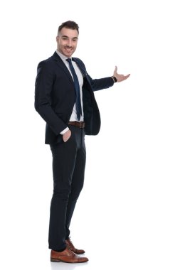 Beyaz stüdyo arka planında dururken gülümseyen ve sunan kendinden emin iş adamının yan görüntüsü