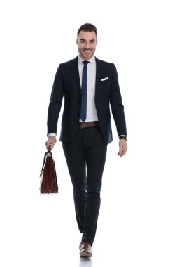 Beyaz stüdyo arka planında yürürken mutlu bir işadamı evrak çantası tutuyor ve gülümsüyor.