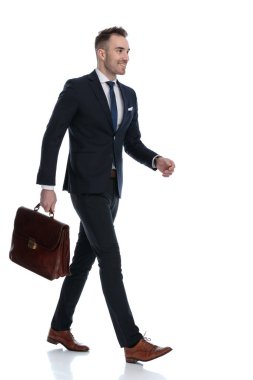 Beyaz stüdyo arka planında yürürken elinde evrak çantası ve gülümseyen mutlu işadamının yan görüntüsü