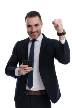 Pozitif iş adamı beyaz stüdyo arka planında dururken kutlama yapıyor ve cep telefonunu tutuyor