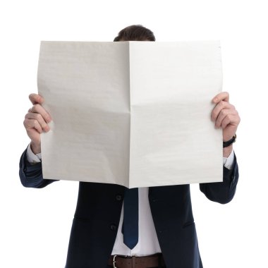 Genç iş adamı, beyaz stüdyo arka planında dikilirken yüzünü gazeteyle örtüyor.