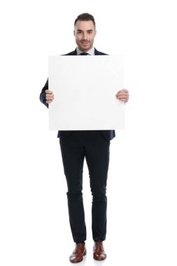 Pozitif iş adamı beyaz stüdyo arka planında dururken gülümsüyor ve elinde boş bir reklam panosu tutuyor.