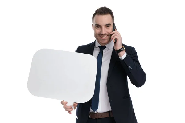 微笑的商人拿着话筒站在白工作室的背景下在手机上聊天 — 图库照片