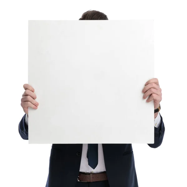 若いビジネスマンが白いスタジオの背景に立っている間 彼の顔を空白の看板で覆います — ストック写真