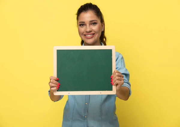 Positive Casual Woman Presenting Blackboard Smiling While Standing Yellow Studio — Stock Photo, Image