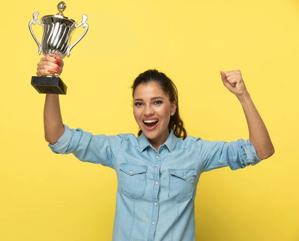拿着奖杯庆祝的快乐而随意的女人 站在黄色工作室的背景上喊叫着 — 图库照片