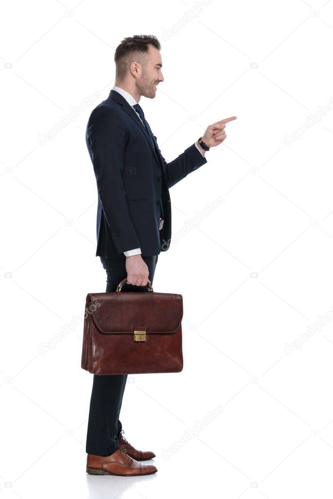 Side view of happy businessman holding briefcase and pointing while standing on white studio background