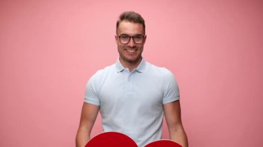 Genç, yakışıklı, sıradan bir adam büyük kırmızı kalbini yavaşça kaldırıyor ve pembe arka planda kameraya gösteriyor.