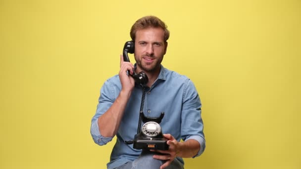 年轻的生意人把一部复古电话放在膝上 在黄色的背景上谈笑着 — 图库视频影像