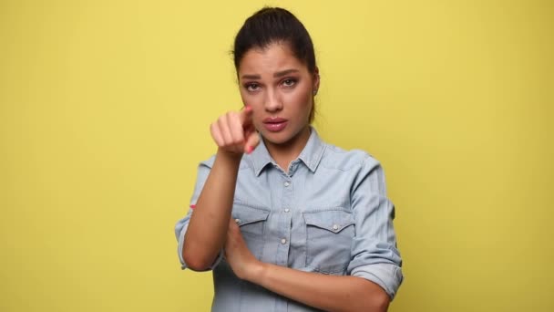 青いデニムシャツを着た若いカジュアルな女性が腕を折ったり指を指差したり黄色の背景を拒否したり — ストック動画