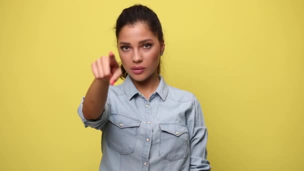 青いデニムシャツを着たカジュアルな若い女性が指を指してジェスチャーをせず 黄色の背景で拒否し うなずいて — ストック動画