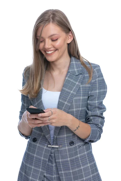 身穿蓝色格子西装 充满热情的年轻女性 手持电话 阅读邮件和发短信 面带微笑 孤身一人站在白色背景下 — 图库照片