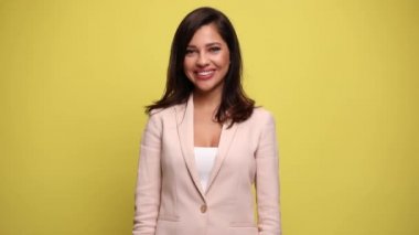 Güzel iş kadını kameraya gülümsüyor ve sarı arka planda iki eliyle baş parmağını kaldırıyor.