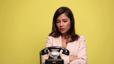 Seksi iş kadını kollarını eski bir telefonun yanında kavuşturmuş, çalmayı bekliyor, çıldırıyor ve işaret ediyor. Neden beni sarı arka plandan aramıyor?