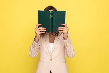Pembe takım elbiseli genç iş kadını kitabın arkasına saklanıyor ve beyaz arka planda tek başına duruyor.