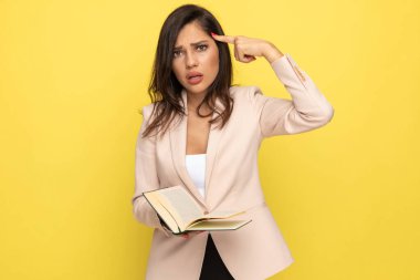 Pembe elbiseli rahatsız genç bir kadın parmak uçlarına basıyor, kitap okuyor ve sarı arka planda poz veriyor.