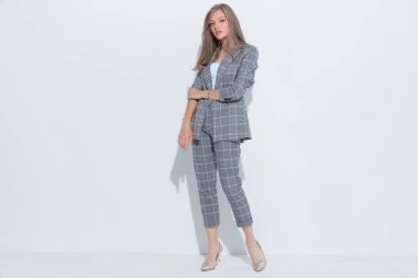 Kendine güvenen moda işkadını beyaz stüdyo arka planında dikilirken kollarını düzeltiyor ve takım elbise giyiyor.