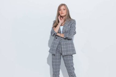 Kendine güvenen moda işkadını, beyaz stüdyo arka planında dururken el ele tutuşup takım elbise giyiyor.