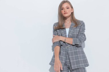 Ciddi bir moda işkadını, beyaz stüdyo arka planında dikilirken takım elbise giyiyor.