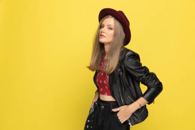 Çekici manken iki elini de cebinde tutuyor, sarı stüdyo arka planında duruyor.