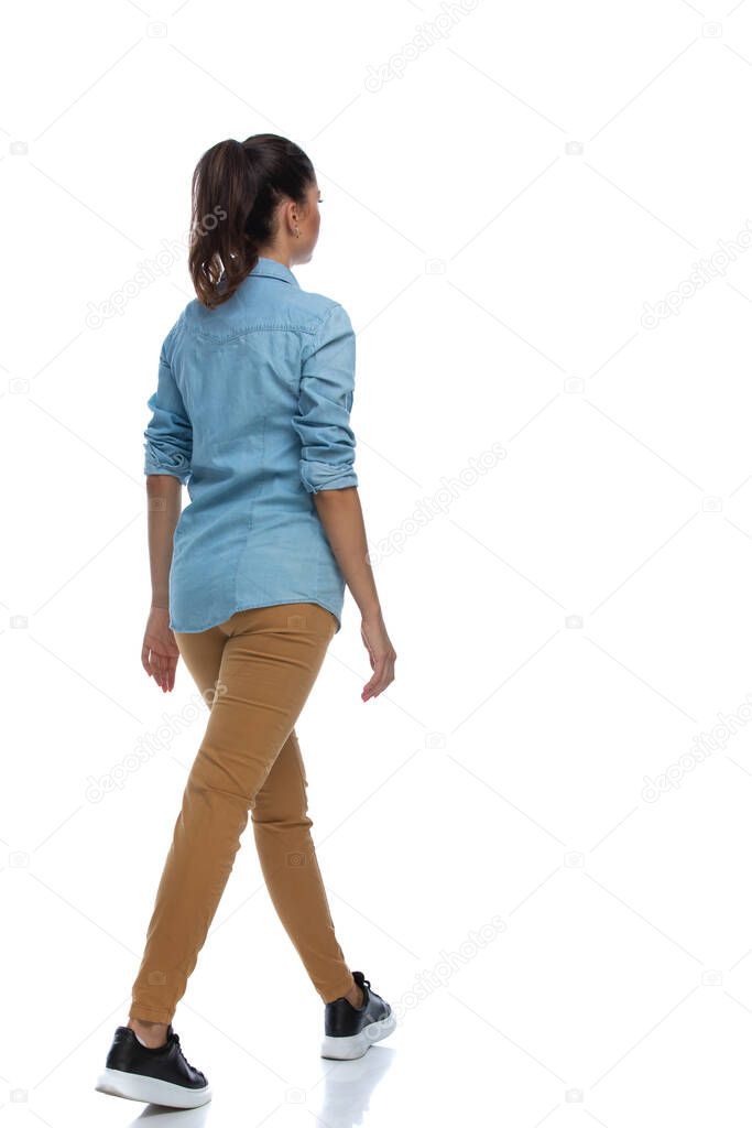 Side rear view of smart casual woman walking and wearing shirt on white studio background
