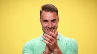 Alkışlayan ve sarı arka planda kamerayı gösteren çekici bir adam.