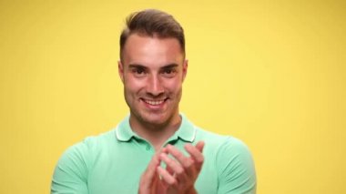 Sıradan bir adam ellerini çırpıyor, minnettarlığını gösteriyor, kamerayı işaret ediyor ve sarı arka plandaki başarıları kutluyor.