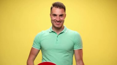 Yakışıklı, sıradan bir adam büyük kırmızı kalbini kaldırıyor ve onu sarı arka planda kameraya gösteriyor.