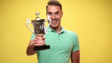 Genç, çekici, sıradan bir adam ödülünü yükseltiyor ve sarı arka planda başarıları kutluyor.