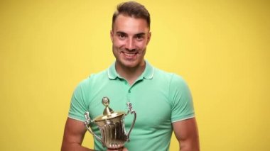 Genç, seksi, sıradan bir adam bardağını tutuyor, kendini işaret ediyor ve sarı arka planda zaferi kutluyor.