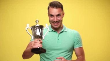 Sıradan bir genç adam fincanını gösteriyor ve sarı arka plandaki kamerayı işaret ediyor.