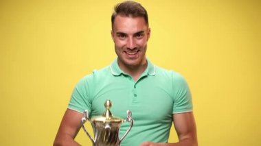 Sıradan yakışıklı bir adam kadehini kaldırıyor, kamerayı işaret ediyor, kendini işaret ediyor, sarı arka plandaki başarıları kutluyor.