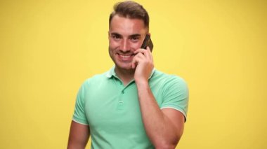 Genç adam telefonda konuşuyor, gülümsüyor, duyduklarına şaşırıyor ve sarı arka planda gülüyor.