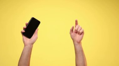 İki kol bir cep telefonu tutuyor, kamerayı işaret ediyor, beni işaret ediyor ve sarı arkaplanı işaret ediyor.
