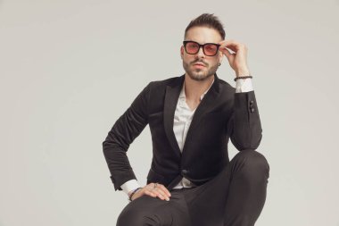 Güneş gözlüğünü ayarlarken gri stüdyo arka planında çömelmiş büyüleyici bir manken.
