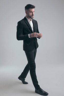 Dalgın zarif adam şaşırmış, takım elbiseli ve gri stüdyo arka planında yürüyor.