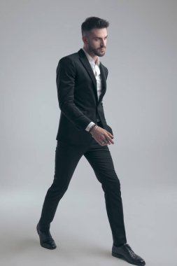 Yakışıklı, zarif takım elbiseli ve gri stüdyo arka planında yürüyen bir adam.