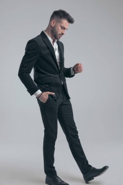 Gri stüdyo arka planında yürürken cebinde takım elbisesi olan zarif bir adam.