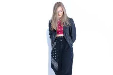 Üzgün manken suçlu gibi görünüyor, beyaz stüdyo arka planında dururken gözlük ve deri ceket giyiyor.