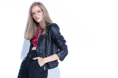 Beyaz stüdyo arka planında dururken el ele tutuşan, gözlük takan ve deri ceket giyen kararlı bir manken.