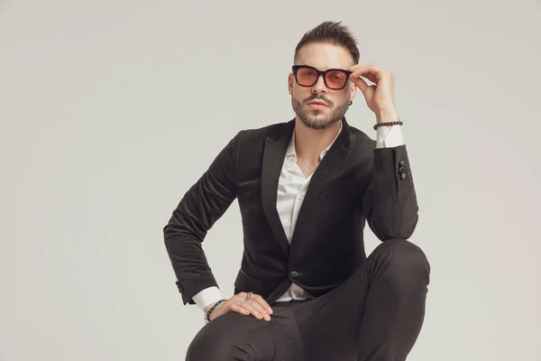 Charming Fashion Model Adjusting His Sunglasses While Crouching Gray Studio — Stock Photo, Image