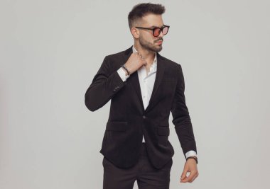 Kendine güvenen manken tasması takıyor ve başka tarafa bakıyor. Gri stüdyo arka planında dururken güneş gözlüğü takıyor.