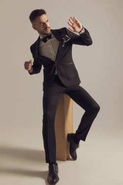 Damat, gri stüdyo arka planında otururken smokin giyip greve hazırlanıyor.